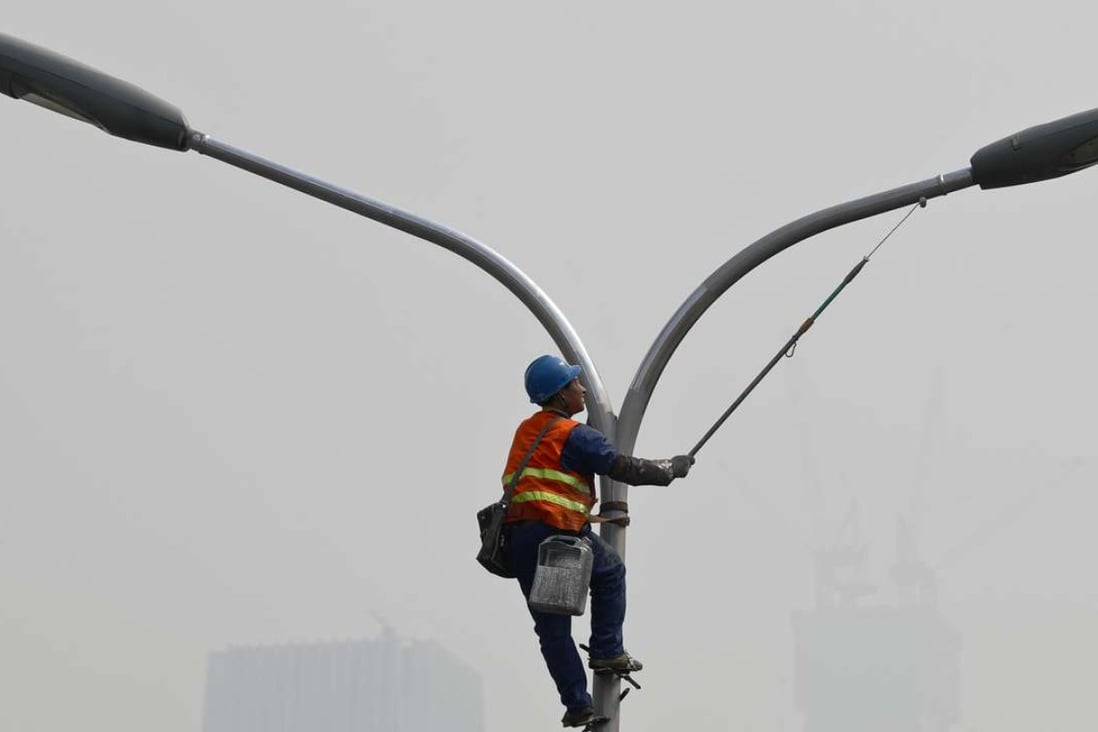 A worker refurbishes a lamp post in Beijing as the capital is blanketed by heavy smog on Monday. Photo: AP