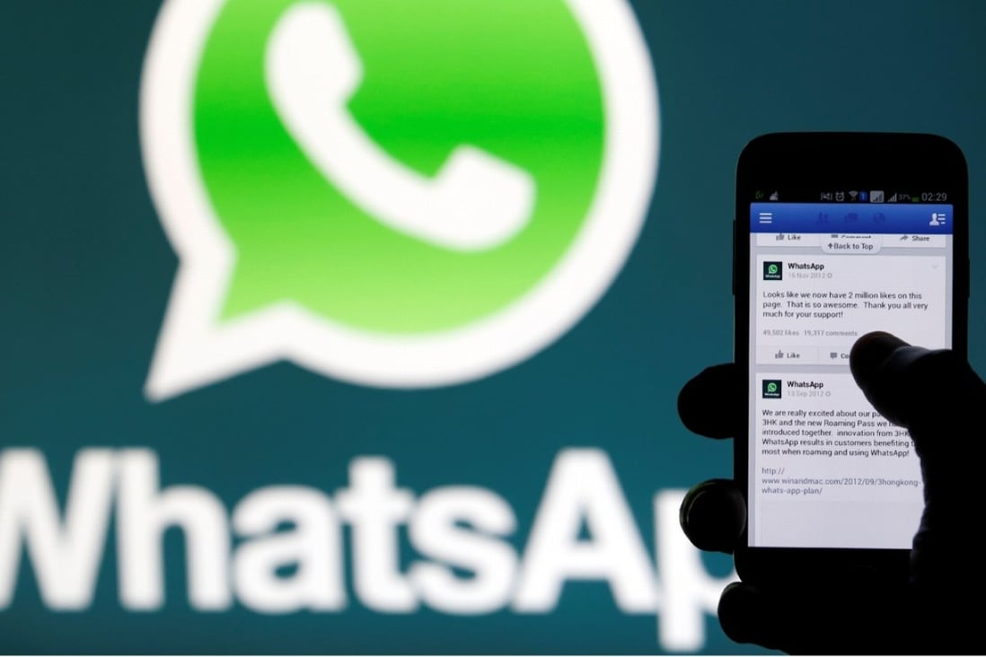 A WhatsApp logo is seen behind a phone that is logged on to Facebook. The popular messaging system was down worldwide for several hours on Wednesday. Photo: Reuters