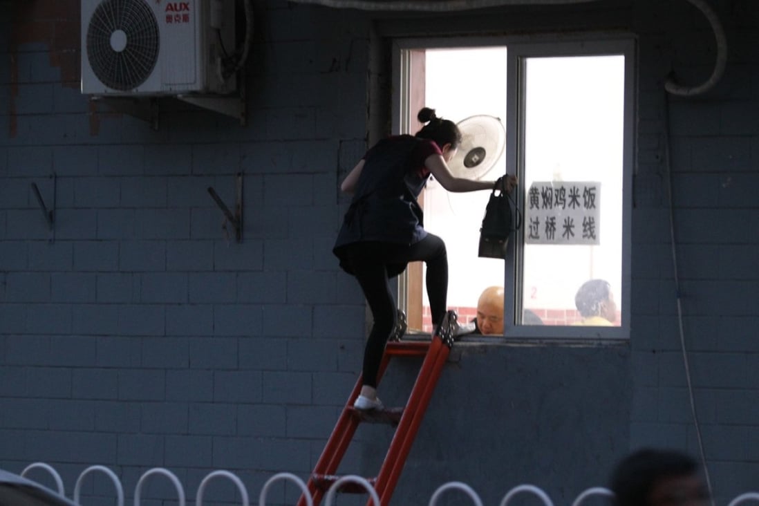 A woman climbs a ladder to enter a small Beijing restaurant via a window on May 10. Photo: Simon Song