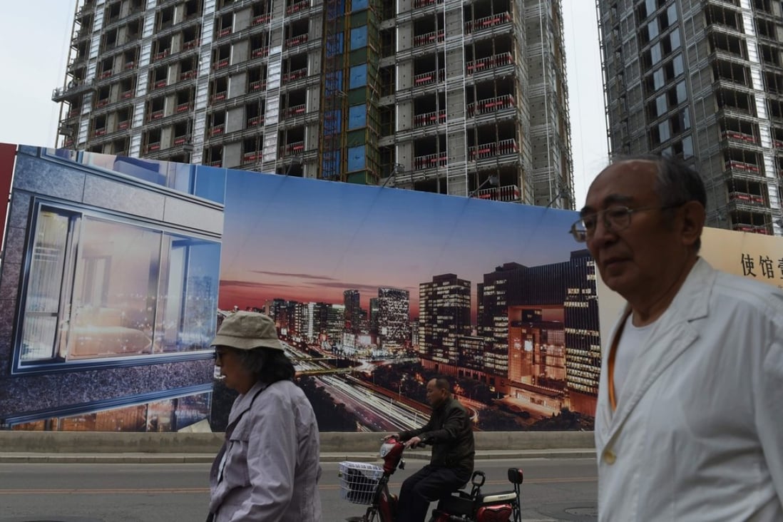 People walk past a billboard advertising a new housing complex outside a construction site in Beijing in May last year. Photo: AFP
