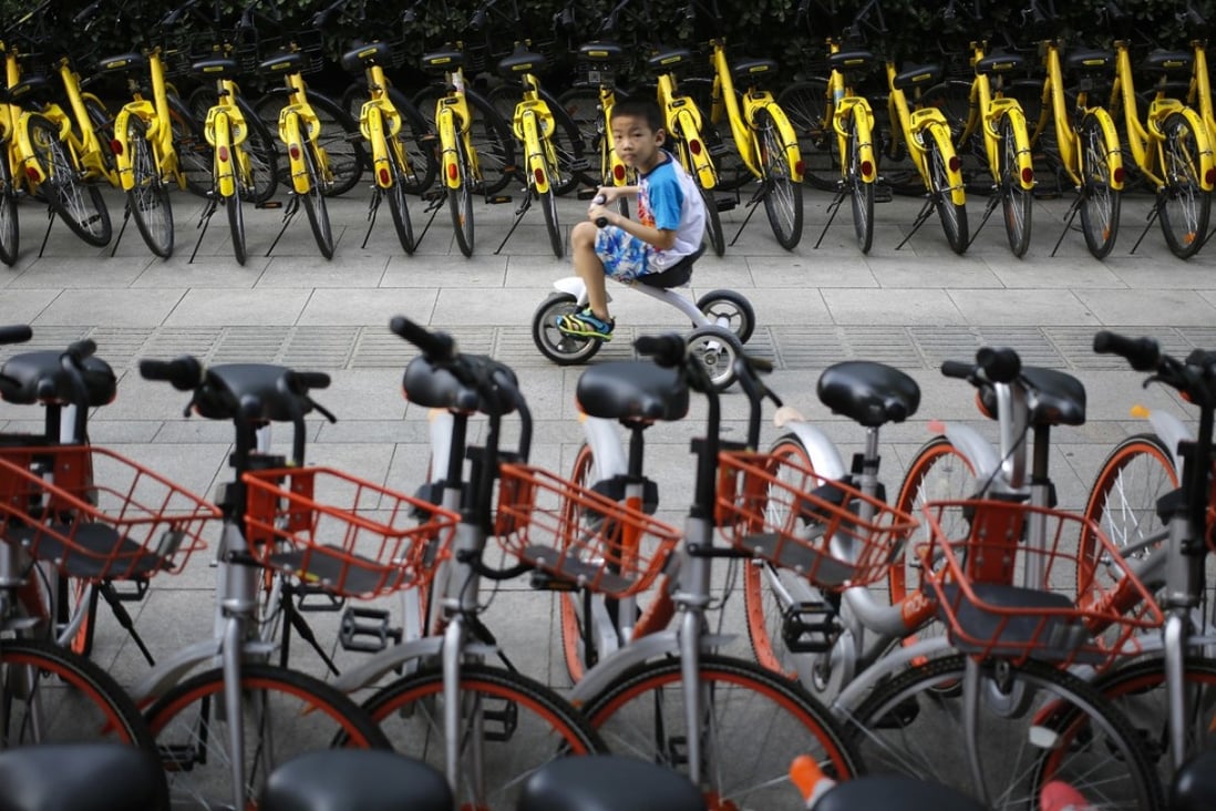 A child rides a bicycle past others from bike-sharing companies parked along a sidewalk in Beijing . (AP Photo/Andy Wong)