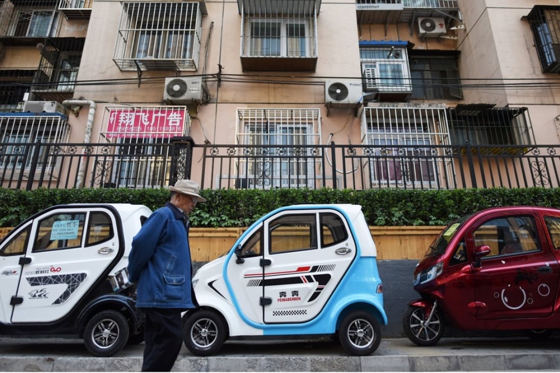 A man walks past electric cars parked on a street in Beijing. Photo: AFP