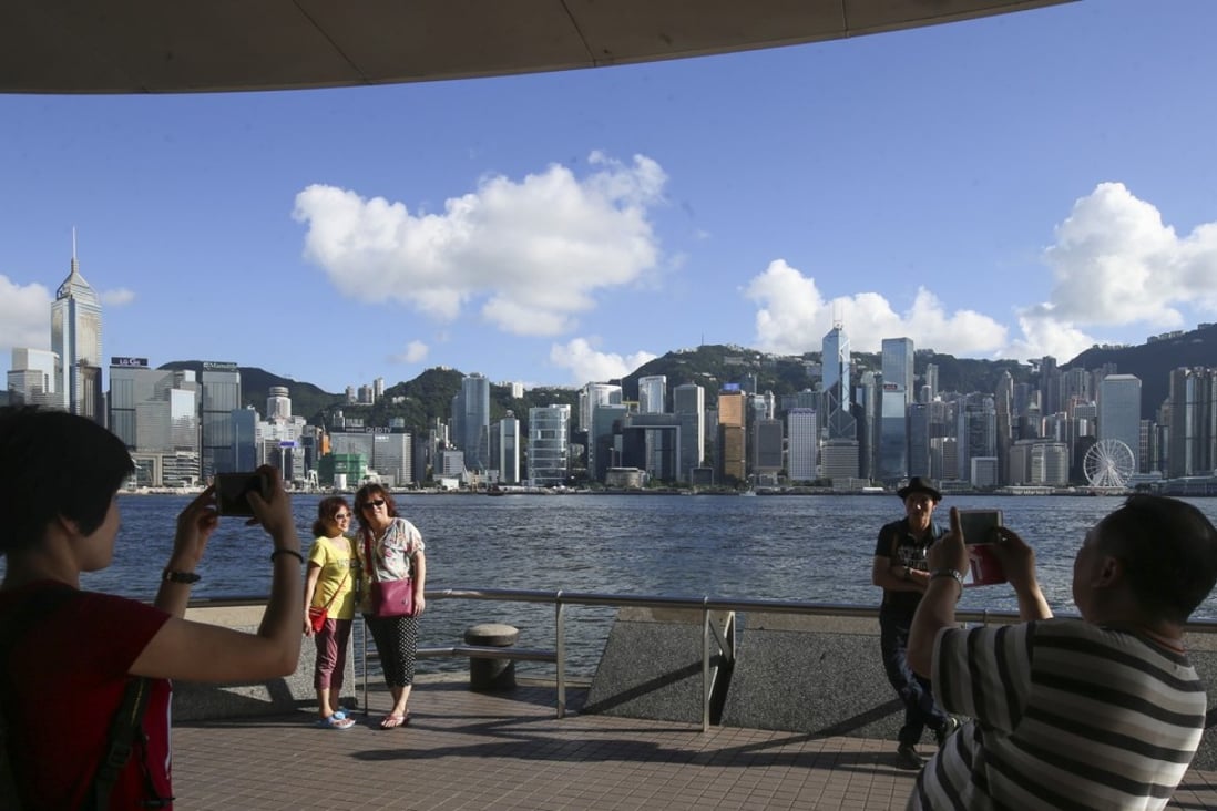 Tourists taking pictures in front of the Victoria Harbour on a sunny day at Tsim Sha Tsui waterfront. David Wong