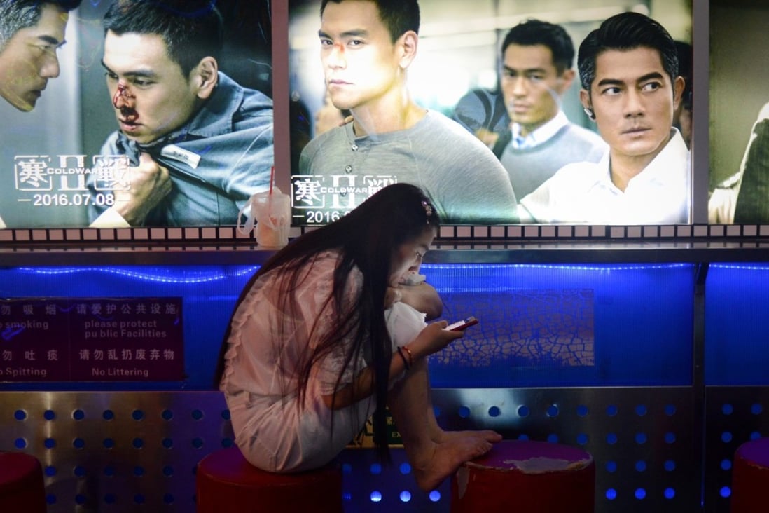 A woman looks at her smartphone at the entrance of a cinema in Beijing. Photo: Agence France-Presse