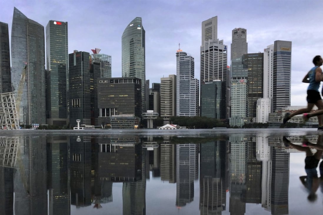 The financial skyline of Singapore is reflected in a rain puddle as people jog past at dawn in Singapore. Photo: AP