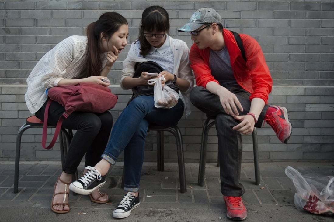 A Chinese woman uses her smartphone as she sits with two friends on a street in Beijing. Photo: AFP