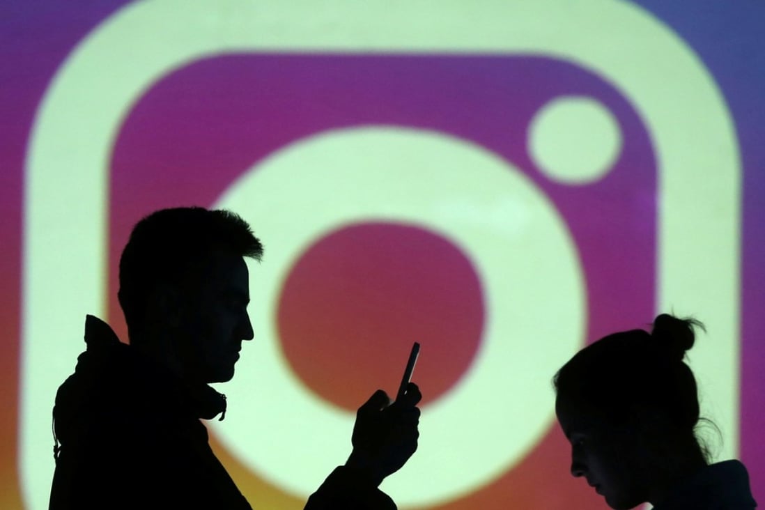 Silhouettes of mobile users are seen next to a screen projection of Instagram’s logo. Photo: Reuters