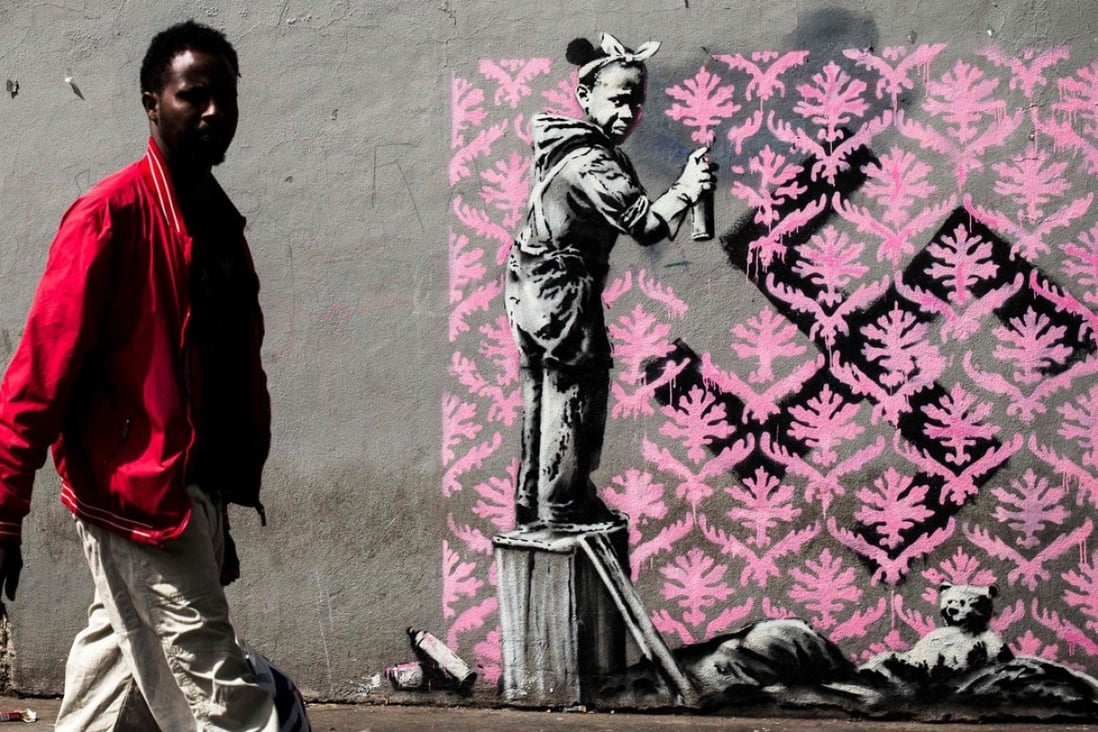 A recent artwork by Banksy in Paris show a young black girl spraying a pink wallpaper pattern over a swastika on a wall next to her sleeping bag and teddy bear. Photo: AFP/Banksy