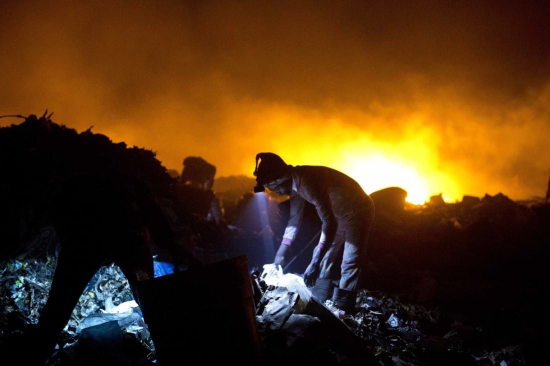 Scavengers work with head lamps as they look for useful items to use or sell at the Truitier landfill, as trash burns behind them in the Cite Soleil slum of Port-au-Prince, Haiti. Photo: AP