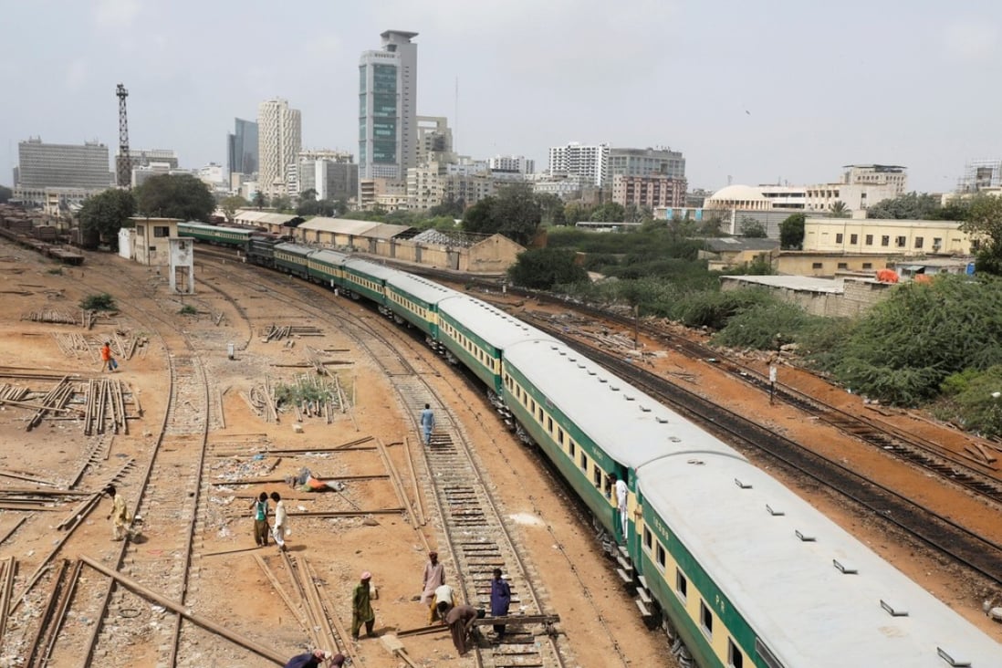 A passenger train passes labourers working on a railway track near City Station in Karachi. Photo: Reuters