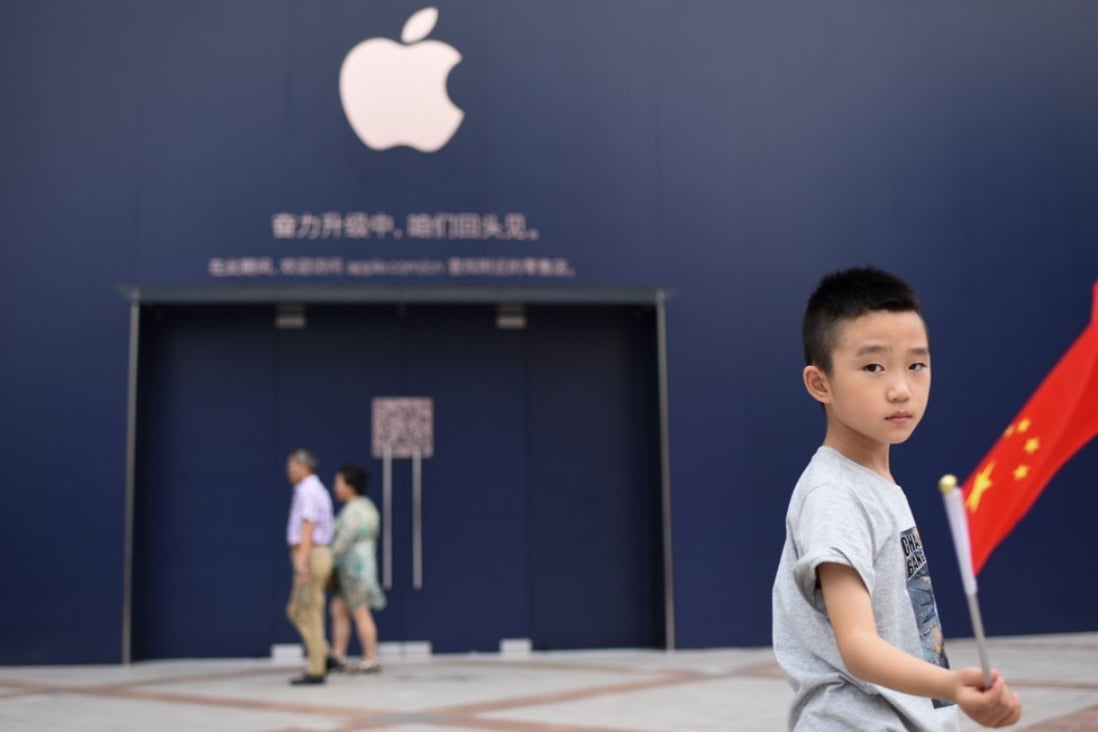 A boy holds a Chinese flag as he walks past an Apple Store undergoing renovation in Beijing on July 18, 2018. Photo: AFP