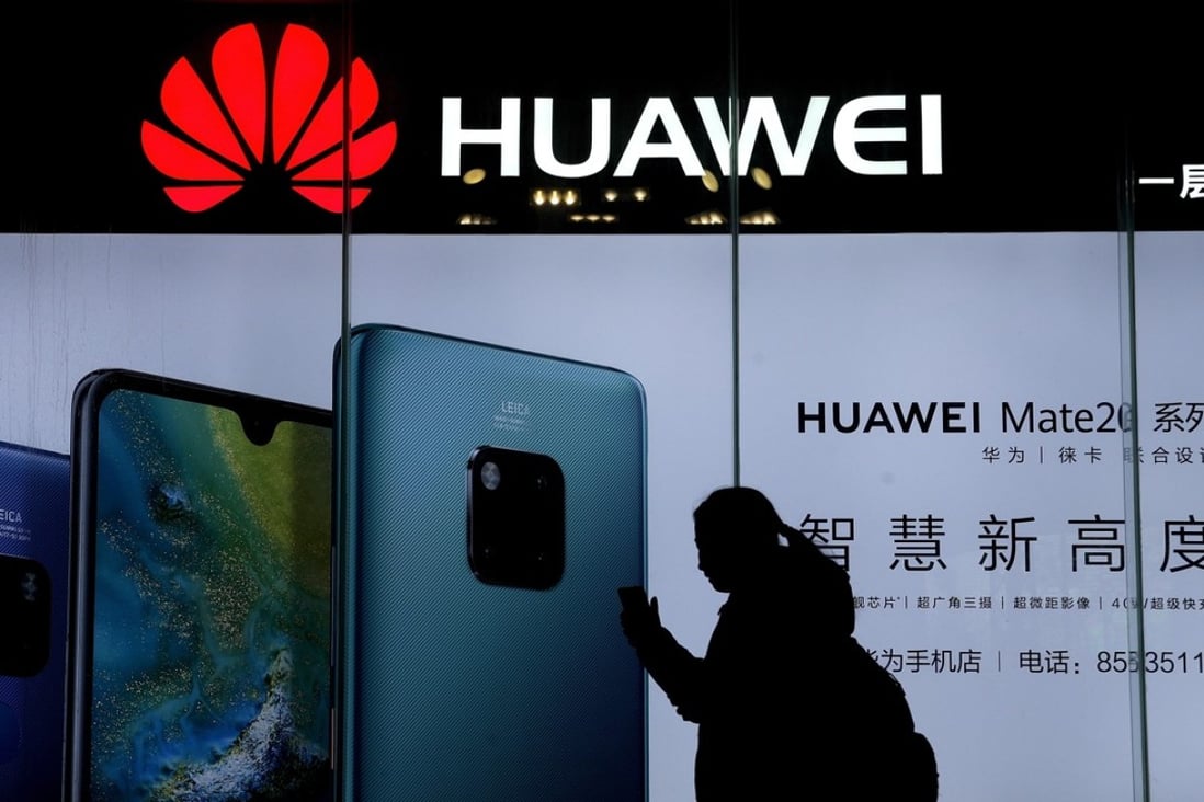 A woman browses her smartphone as she walks by a Huawei store at a shopping mall in Beijing. Photo: AP