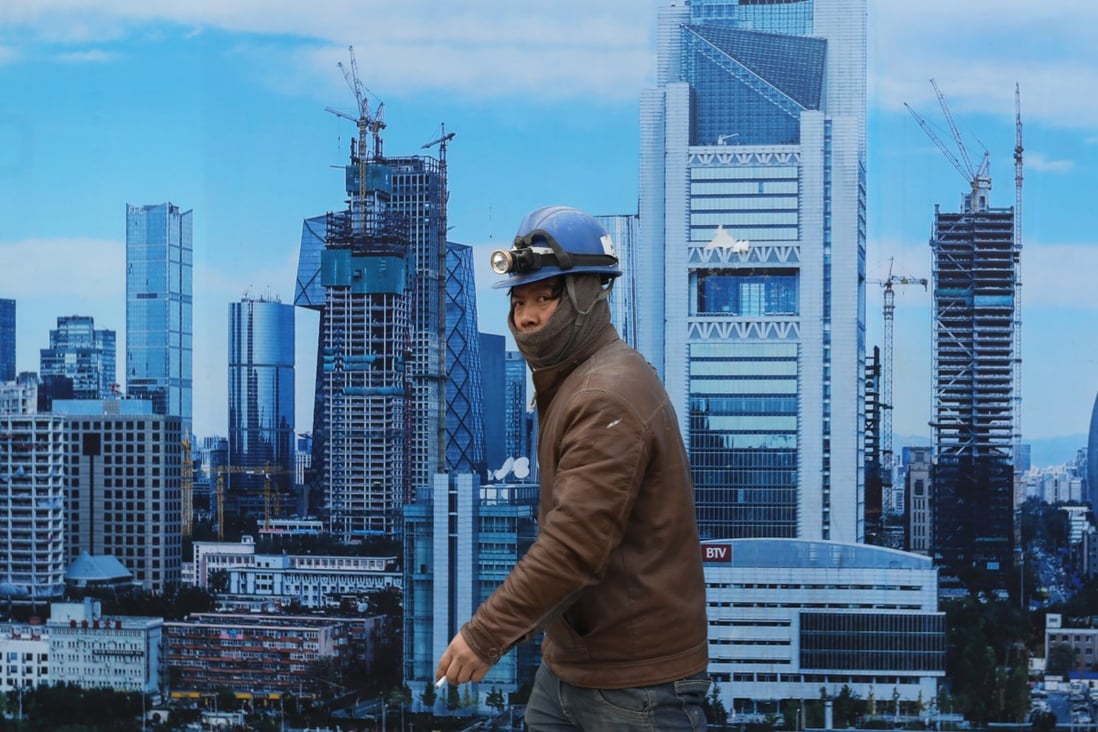 A Chinese migrant worker walks past a poster placed outside of a construction site showing the design of future high-raise buildings and skyscrapers in the central business district in Beijing. Photo: EPA