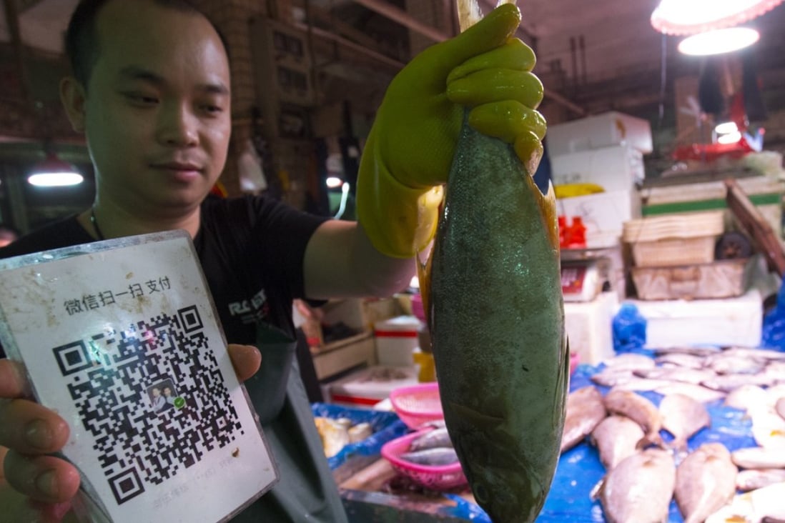 A fish vendor in China holding a QR code to accept mobile payments (Picture: May Tse)