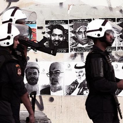 Bahraini riot policemen search for anti-government protesters during clashes in Sitra on Monday. Pictures of jailed political leaders behind last year's uprising and people killed in the ensuing unrest are plastered on the wall. Photo: AP