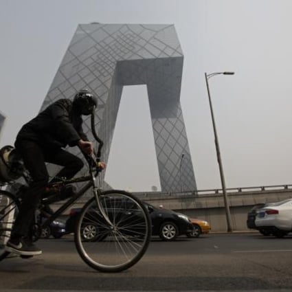 Artist Matt Hope, wearing a helmet linked to his air filtration bike, rides past the China Central Television (CCTV) building on a hazy day in Beijing. Photo: Reuters