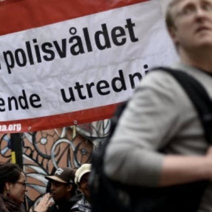 A man passes by a banner reading "Stop police violence for an independent investigation" during a demonstration against police violence and vandalism in the Stockholm suburb of Husby. Photo: AFP