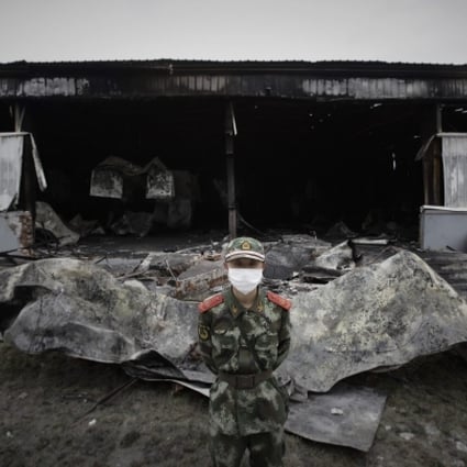 A paramilitary policeman wearing a mask stands guard in front of the burnt-out site of a poultry slaughterhouse in Dehui. Photo: Reuters