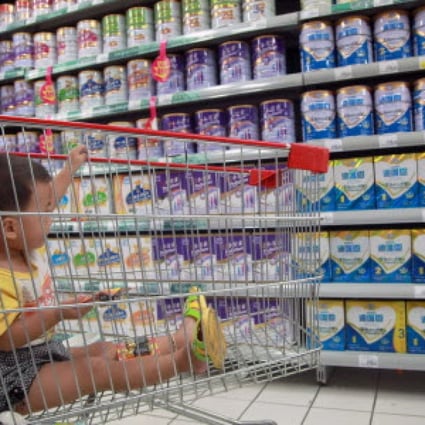 A baby stays in a shopping cart as his mother selects baby milk in a supermarket. Chinese mothers have signalled a continuing preference for foreign brands even after the Fonterra scandal. Photo: AFP
