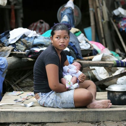 A mother holds her one-month-old daughter outside the remains of her damaged house in San Miguel town, Bulacan province. Photo: AP