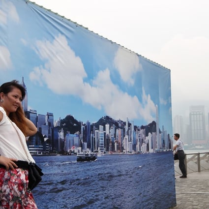 A tourist from mainland poses for photo in front of a large outdoor banner with an image of the Hong Kong island skyline at the waterfront in Tsim Sha Tsui. Photo: Sam Tsang