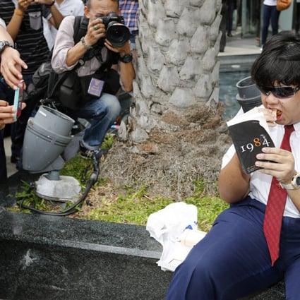 A Thai anti-coup protester eats a sandwich as he reads a book as a sign of protest outside a shopping centre in Bangkok. Photo: EPA