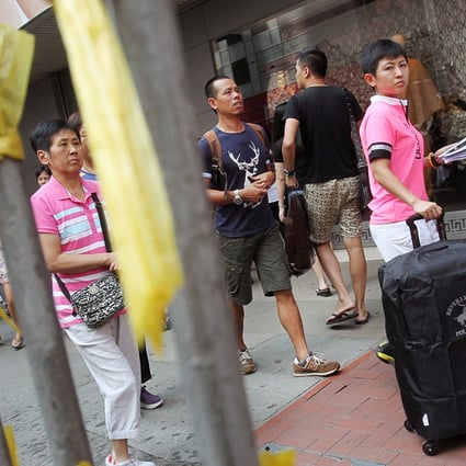 Mainland tourists pass an Occupy Central sign in Causeway Bay yesterday. Fewer mainlanders will be visiting the city after package tours were suspended. Photo: May Tse
