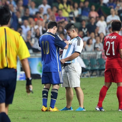 Two-goal Lionel Messi signs the shirt of a delighted pitch invader. Photo: K. Y. Cheng