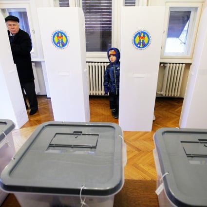 A Moldovan man (left) votes while being watched by a young boy during  Moldova's parliamentary elections, at a polling station organised at Molodva's embassy in Bucharest. Photo: EPA