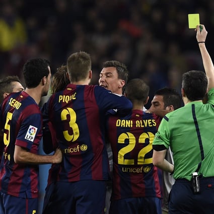 Players from Barcelona and Atletico argue as the referee hands out a yellow card. Photo: AFP