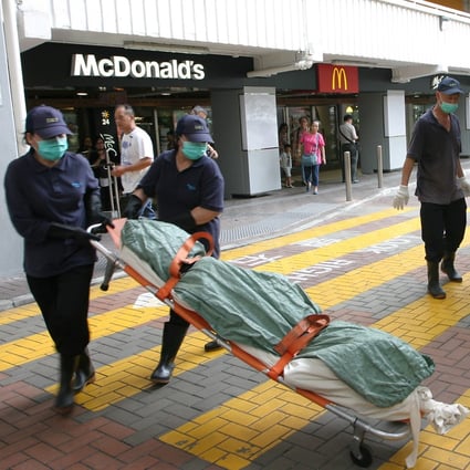 Workers remove the body of the homeless woman from the Ping Shek Estate McDonald's in Kowloon Bay on Sunday. Photo: SCMP Pictures