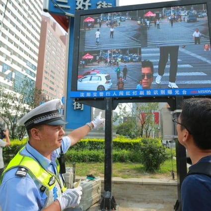 A policeman shows a man that he's been caught jaywalking on a screen besides a road in Shenyang. (Source: China Foto Press)