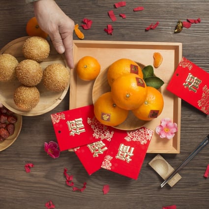 Flat lay Chinese lunar new year food preparation table top shot. Senior female hand serving a plate of sesame ball dessert on wooden table. Chinese word “Blessing” printed on red packet. Photo: Getty Images