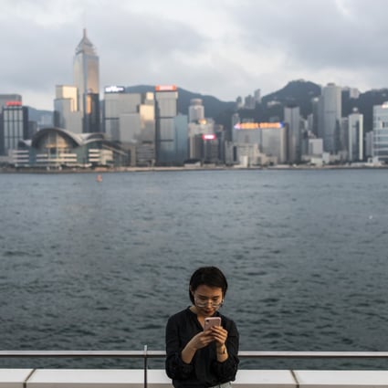 A woman uses a smartphone along Victoria Harbour in Tsim Sha Tsui on April 29, 2019. The financial secretary has announced a raft of measures to boost information and technology in Hong Kong. Photo: Bloomberg