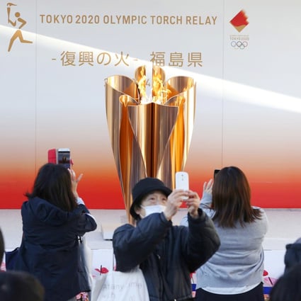 People wearing masks take pictures of the Olympic flame exhibited in Fukushima on March 24, 2020, before the Tokyo 2020 Olympic Games were postponed for a year. Photo: Kyodo