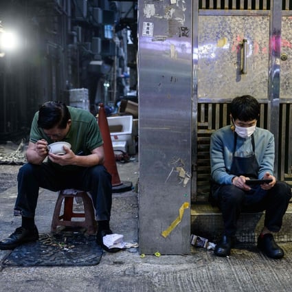 A man eats dinner in an alley as another man checks his phone in Hong Kong on January 4. Photo: AFP 