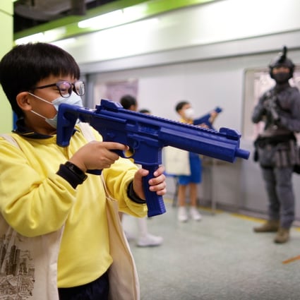 Children play with toy guns as a member of the Railway Response Team looks in a model of a Hong Kong MTR station during an open day to mark National Security Education Day. Photo: Reuters