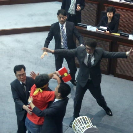 Leung Kwok-hung, in red, is stopped by security guards as he tries to throw a plastic hammer towards then chief secretary Carrie Lam Cheng Yuet-ngor (seated far left) during a meeting on proposed electoral reforms, at the Legislative Council in Hong Kong on July 15, 2014. Photo: Sam Tsang