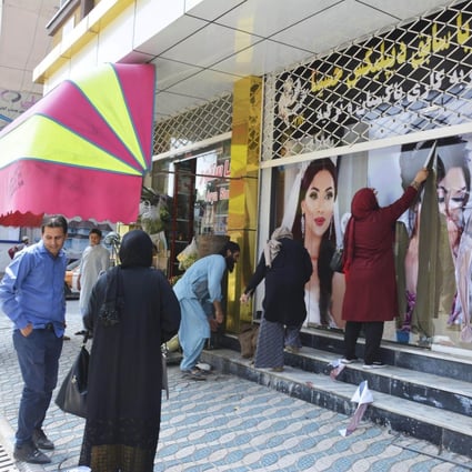 Workers at a beauty salon strip large images of women off the wall in Kabul on August 15 following news that the Taliban had swept into the Afghan capital. Photo: Kyodo