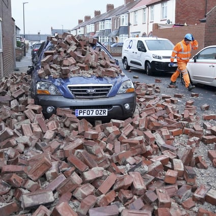 A man in the north of England walks past a car lying under fallen bricks after powerful wind gusts battered Britain during “Storm Arwen”. The Met Office issued a rare red warning for wind from 3pm on Friday to 2am on Saturday. Photo: PA via AP
