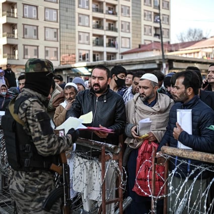 A Taliban fighter inspects documents of people queuing to enter the passport office in Kabul, Afghanistan, on December 18. Photo: AFP
