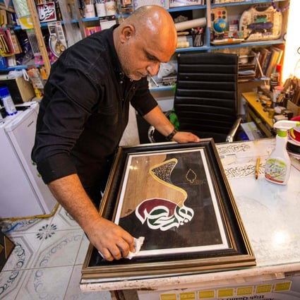 Iraqi calligrapher Wael al-Ramdan wipes the glass on one of his Arabic calligraphy framed art pieces at his workshop, in Basra, Iraq. A few dedicated artists are keeping the ancient tradition alive. Photo: AFP