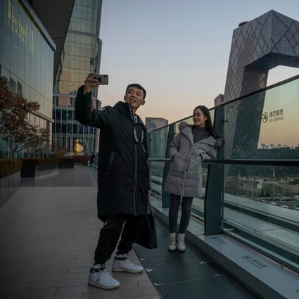 People take a selfie, with the China Central Television Tower as background, in Beijing on  December 13, 2021. China assets are predicted to offer investors stability this year. Photo: Bloomberg