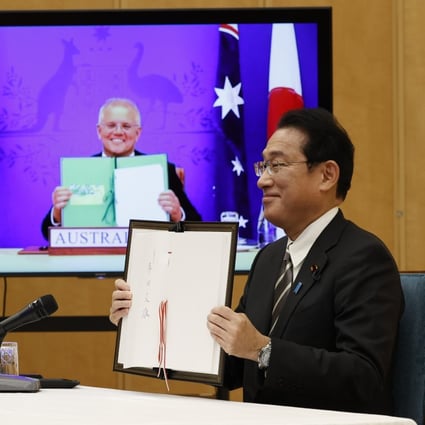 Japan’s PM Fumio Kishida and Australia’s PM Scott Morrison, seen on screen, show off signed documents during a virtual summit to sign the Reciprocal Access Agreement. Photo: AP 