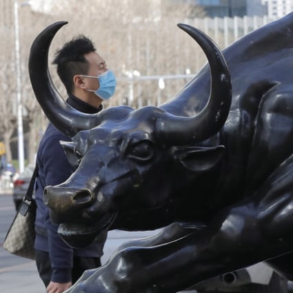 A man wearing a mask walks by a bronze sculpture of a bull in Beijing’s central business district. Photo: EPA-EFE