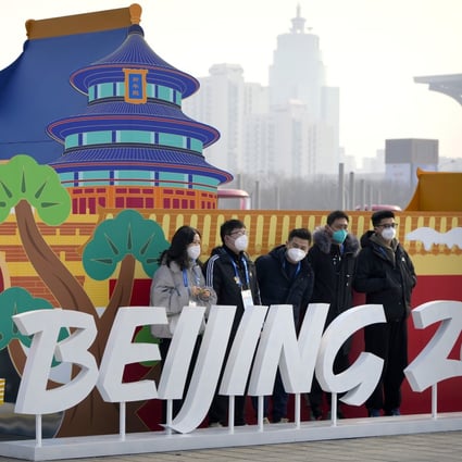 Staff members pose for a group photo with a Beijing 2022 Olympics display on the Olympic Green near the main media centre. Photo: AP