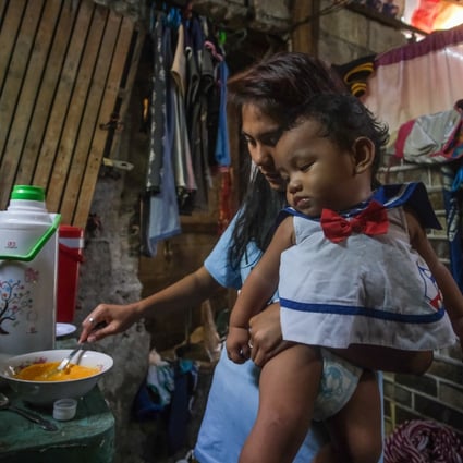 Erlyn, 18, prepares food while holding her baby son. The youngster quit school at 17 after her brother’s sudden death and began working as a masseuse. She then met the man who became her husband and fell pregnant. Photo: Geela Garcia