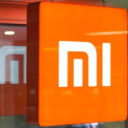 A man looks on his a mobile phone as he stands next to a reflected Xiaomi logo outside a store selling the smarphone brand in Kyiv on October 22, 2018.
