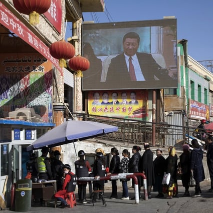 Residents line up at a security checkpoint into the bazaar in Hotan, Xinjiang, where a screen shows Chinese President Xi Jinping. Photo: AP