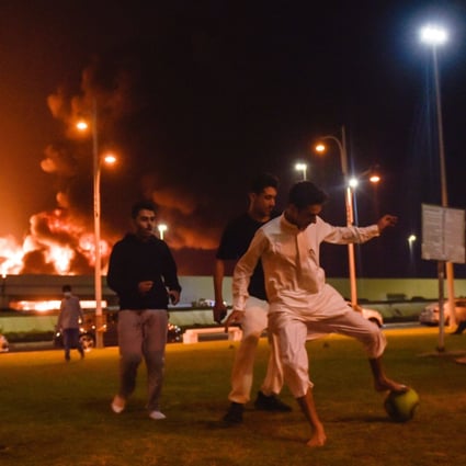 Youngsters in Jeddah play football as smoke and flames rise from a Saudi Aramco oil facility in the distance behind them. Photo: AFP